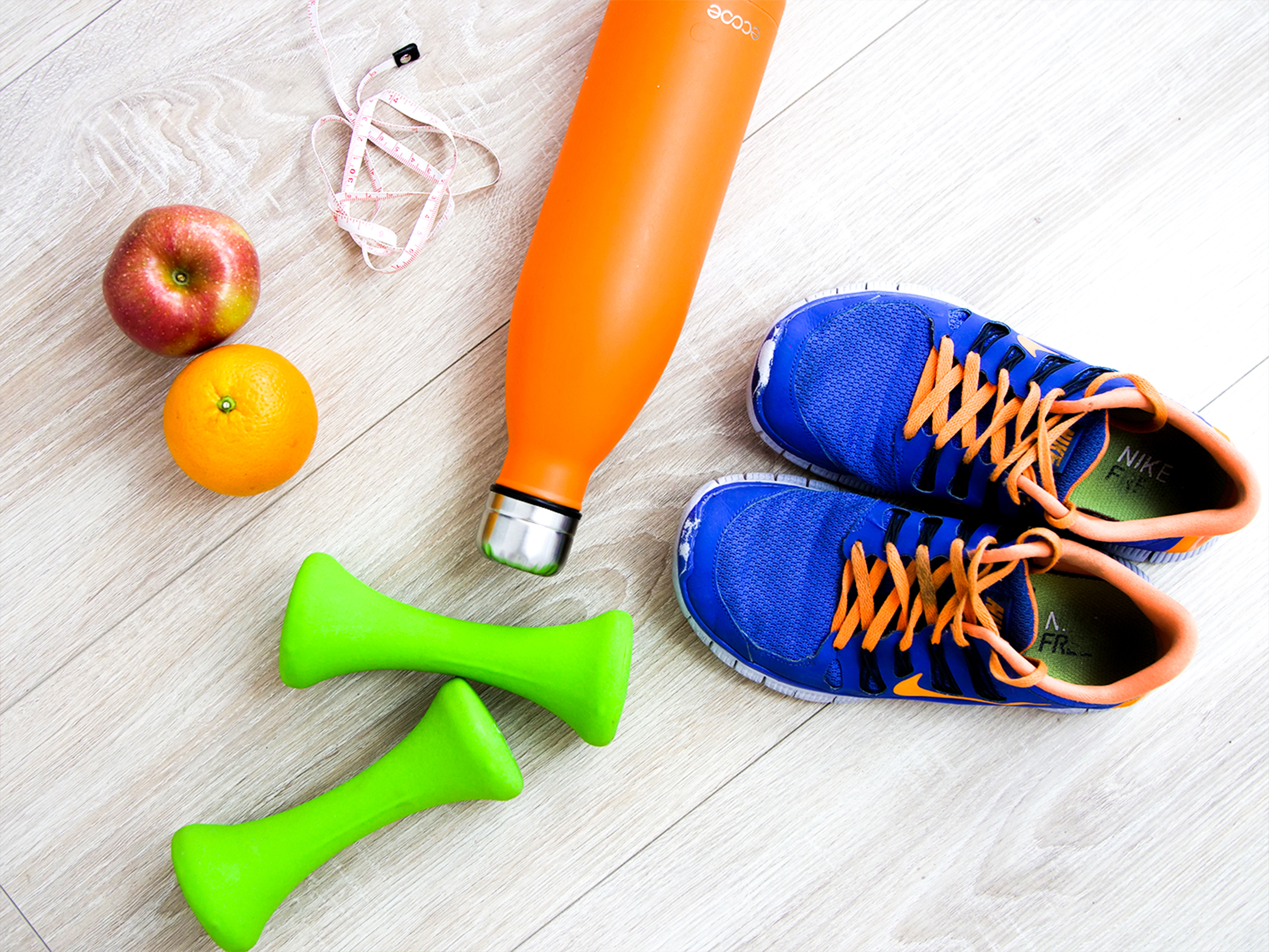 Flat lay view of fruit, a blue sneaker, orange water bottle, a tape measure and green dumbbells