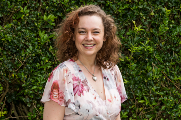Melanie smiling at camera with green bush behind her;