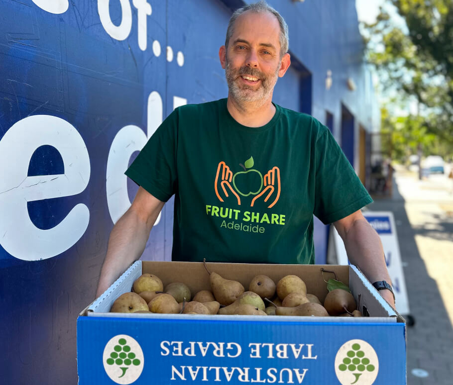 A person wearing a Fruit Share Adelaide t-shirt, holding a cardboard box full of pears